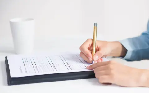 Dłoń pisze złotym długopisem na formularzu, przygotowując wniosek o zatarcie skazania.