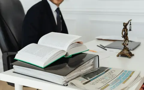 Prawnik w garniturze studiuje kodeks, art. 11 kpk, obok stosu akt i gazety "Dziennik Gazeta Prawna".