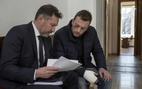 Prawnik omawia z poszkodowanym mężczyzną dokumenty dotyczące artykułu 157 paragraf 2 kodeksu karnego. Mężczyzna ma widoczne obrażenia.