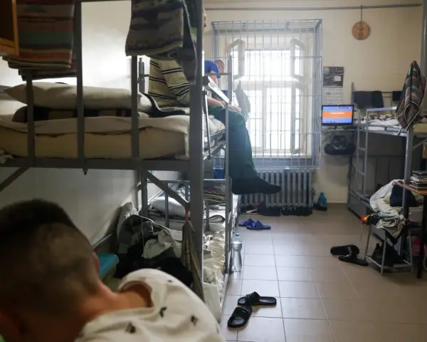Wnętrze celi, areszt śledczy. Dwie osoby na łóżkach piętrowych, okno z kratami, telewizor.