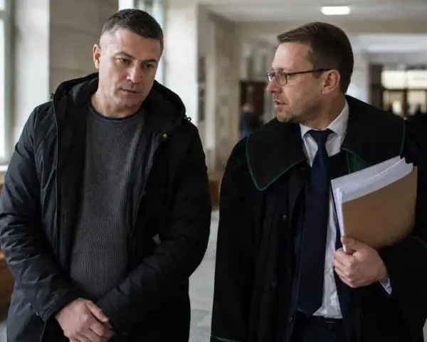 Mężczyzna w czarnej kurtce rozmawia z prawnikiem w todze. Czy usłyszą wyrok w zawieszeniu?