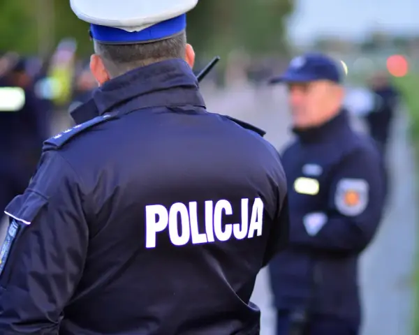 Policjanci w mundurach, jeden z napisem "POLICJA" na plecach, gotowi do akcji. Czy to kontrola osobista, czy przeszukanie?