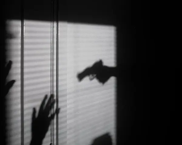 Cień dłoni z pistoletem grozi dwóm dłoniom, które próbują się zasłonić. To scena jak z filmu o świadku koronnym.