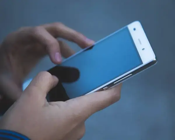 Dłonie trzymają biały smartfon. Czy na dołku można mieć telefon? Tak, nawet w trudnych chwilach można pozostać w kontakcie.
