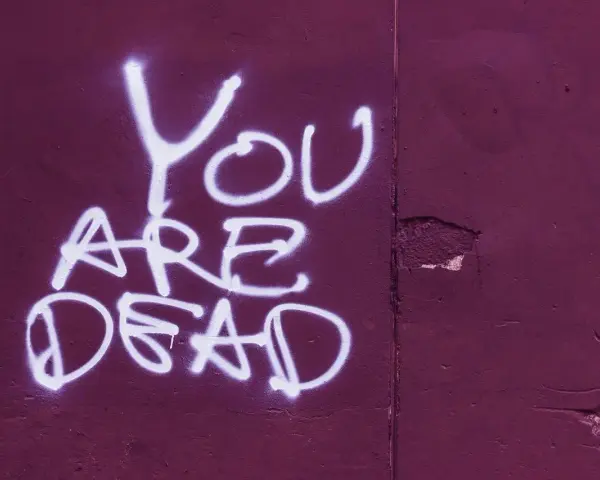 Napis "YOU ARE DEAD" białą farbą na fioletowej ścianie. Groźba jak z artykułu 190 paragraf 1 kk.