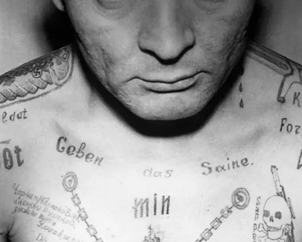 Czarno-białe zdjęcie klatki piersiowej mężczyzny z licznymi tatuażami, w tym swastyką i napisem "Soldat".