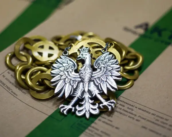 Srebrny orzeł na złotym łańcuchu, leżący na aktach. Symbolizuje prekluzja dowodowa w polskim prawie.