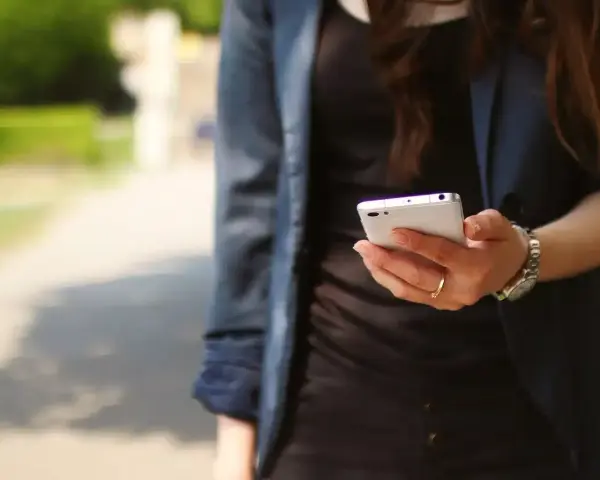 Kobieta z telefonem w dłoni, być może szuka przykładów uporczywego nękania w internecie.