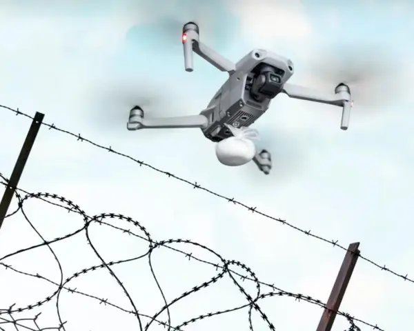 Dron z paczką przelatuje nad drutem kolczastym, niczym rakieta do więzienia dostarczająca przesyłkę.