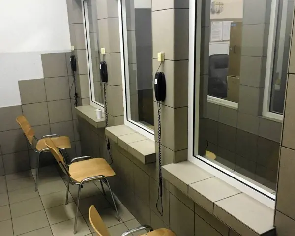 Pokój widzeń w zakładzie karnym półotwartym. Proste krzesła i telefony czekają na rozmowy.