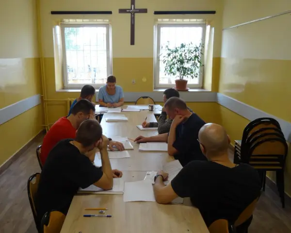 Grupa mężczyzn uczestniczy w zajęciach, które mogą być częścią system programowanego oddziaływania. Siedzą przy stole, studiując dokumenty.