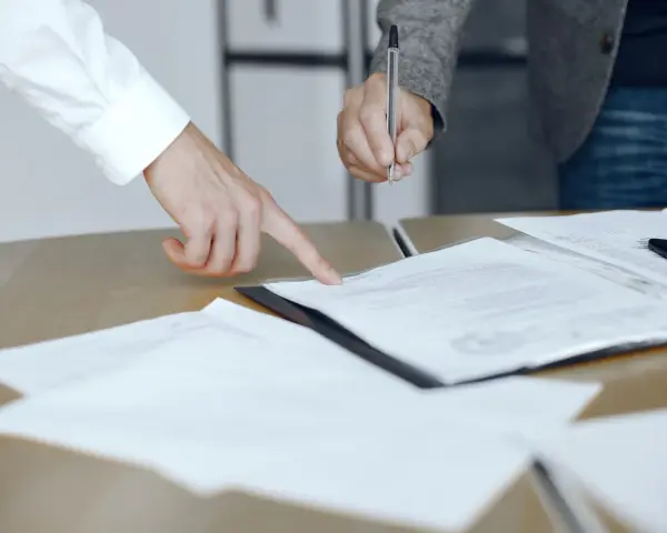 Dwie osoby przy biurku analizują dokumenty. Jedna wskazuje palcem na tekst, druga trzyma długopis, gotowa do podpisania. To może być moment, gdy omawiają, co to jest list żelazny.