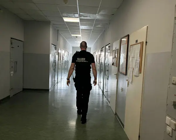 Strażnik więzienny idzie korytarzem, gdzie odbywa się klasyfikacja skazanych. Wzdłuż korytarza znajdują się cele.