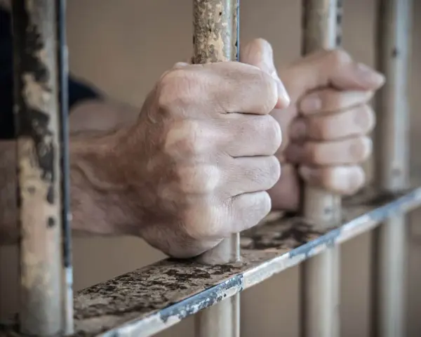Dłonie zaciskają się na kratach aresztu śledczego. Widok zza prętów.