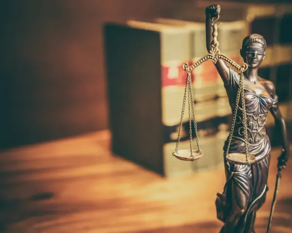 Temida z wagą i mieczem, symbol sprawiedliwości, na tle książek. Jej postawa sugeruje odrzucenie wniosku o wstrzymanie wykonania kary.
