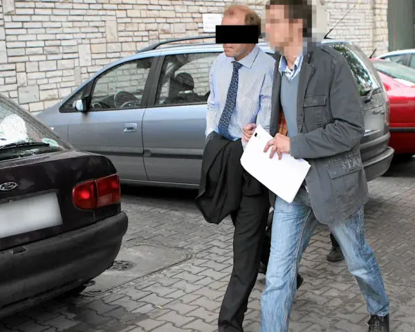Dwóch mężczyzn, jeden w garniturze, drugi w kurtce i jeansach, idzie obok samochodów. Czy to występek, co to za sytuacja?