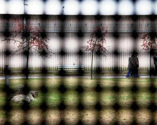 Więzienie w Niemczech. Ludzie spacerują po dziedzińcu, drzewa z czerwonymi liśćmi, ławka, kamień i ogrodzenie.