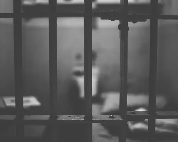 Widok przez kraty więzienne. Ciemne, ponure wnętrze celi, symbolizujące karę pozbawienia wolności.