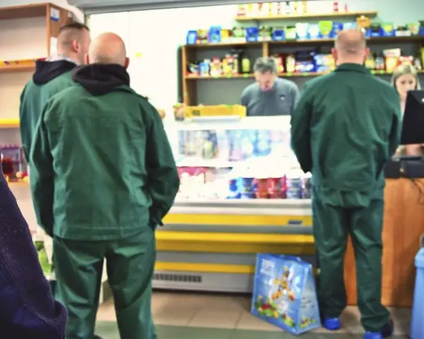 Strażnicy więzienni w zielonych uniformach robią zakupy w więziennej kantynie.