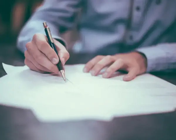 Dłoń pisze długopisem na papierze. Może to być wniosek o obrońcę z urzędu.