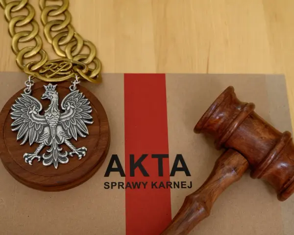 Na brązowej teczce z napisem "AKTA SPRAWY KARNEJ" leży drewniany młotek sędziowski i medalion z orłem RP.