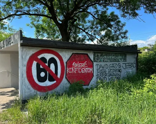 Niedziela, dzień cwel, pod drzewem, z zakazem 60 i napisami na ścianie.