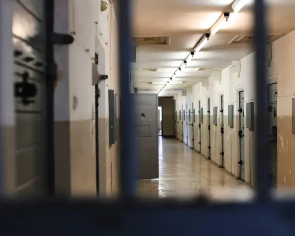 Korytarz więzienny z rzędami cel po obu stronach, widok przez kraty.