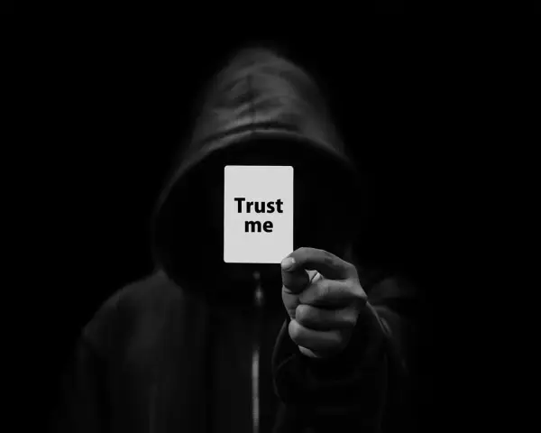 Postać w kapturze trzyma kartkę z napisem "Trust me". To typowy oszustwo, które obiecuje coś, czego nie można spełnić.