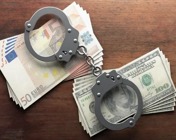 Kajdanki na stosach euro i dolarów. Symbolizują finansowe kk oszustwo i jego konsekwencje.