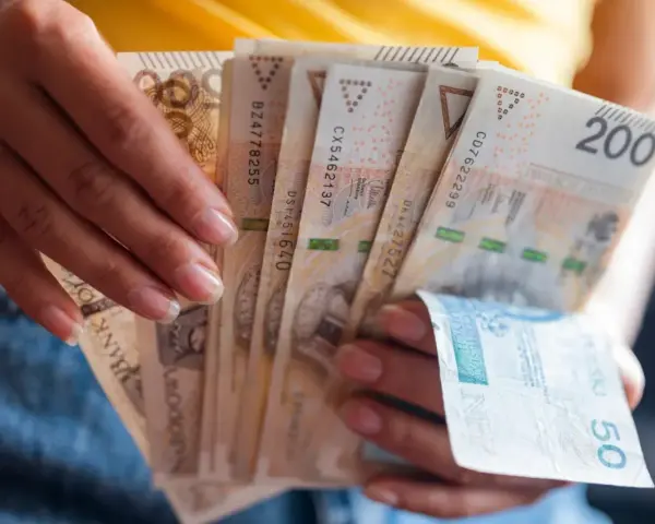 Dłonie trzymają plik banknotów 200 zł i 50 zł. Jak egzekwować obowiązek naprawienia szkody, gdy sprawca nie chce zapłacić?