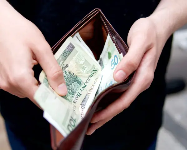 Dłonie wkładają polskie banknoty do portfela. Może to symbolizować rekompensatę za nękanie, która wreszcie trafia do poszkodowanego.
