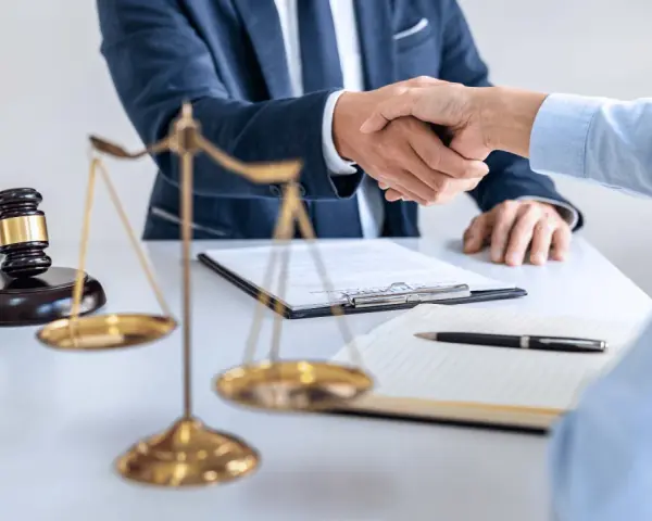 Uścisk dłoni prawników przy biurku z wagą sprawiedliwości i młotkiem. Sprawa 157 kk zakończona sukcesem.