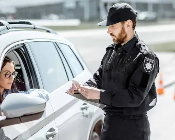 Policjant spisuje dane kierowcy, który może być zagrożony **przepadkiem pojazdu**. Kobieta w okularach siedzi za kierownicą białego samochodu.