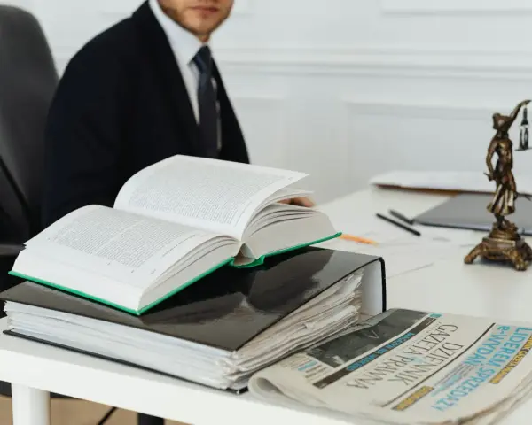 Prawnik w garniturze studiuje kodeks, art. 11 kpk, obok stosu akt i gazety "Dziennik Gazeta Prawna".