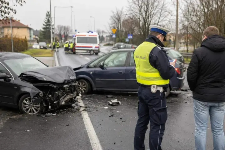 Policjant spisuje notatki po wypadku drogowym. Uszkodzone samochody, art. 177 kk.