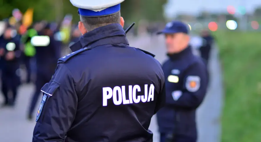 Policjanci w mundurach, jeden z napisem "POLICJA" na plecach, gotowi do akcji. Czy to kontrola osobista, czy przeszukanie?
