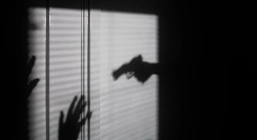 Cień dłoni z pistoletem grozi dwóm dłoniom, które próbują się zasłonić. To scena jak z filmu o świadku koronnym.