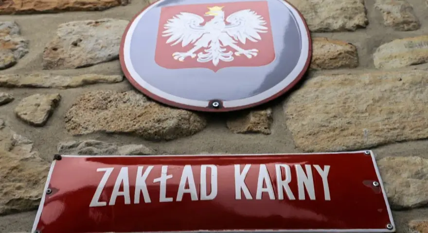 Tablica z napisem "ZAKŁAD KARNY" i godło Polski na kamiennej ścianie.
