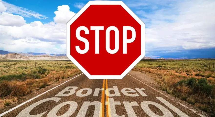 Droga prowadzi przez pustynny krajobraz, a na niej znak STOP i napis "Border Control". To symbol zakazu opuszczania kraju.