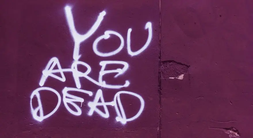 Napis "YOU ARE DEAD" białą farbą na fioletowej ścianie. Groźba jak z artykułu 190 paragraf 1 kk.