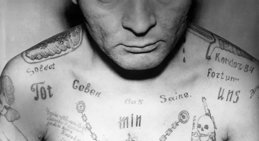 Czarno-białe zdjęcie klatki piersiowej mężczyzny z licznymi tatuażami, w tym swastyką i napisem "Soldat".