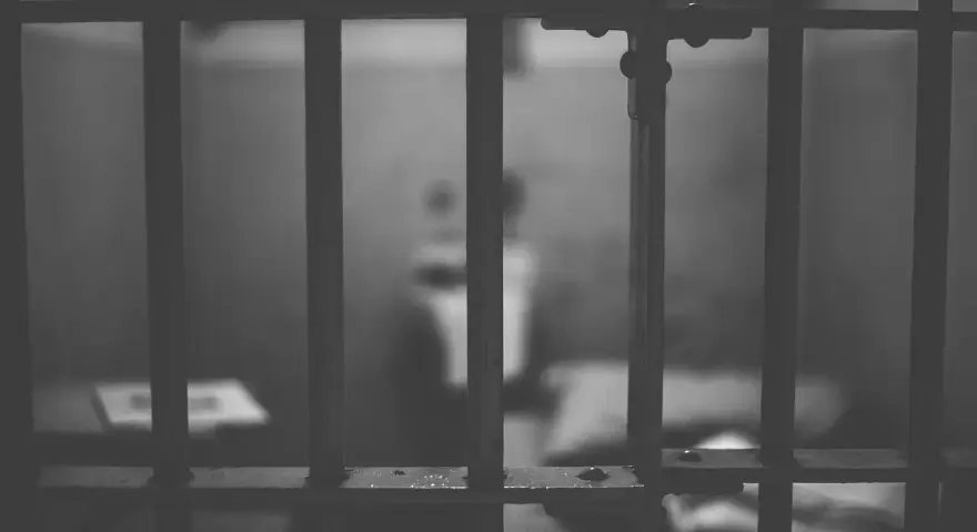 Widok przez kraty więzienne. W tle niewyraźna postać, symbolizująca nadzieję na wcześniejsze zatarcie skazania i nowe życie.