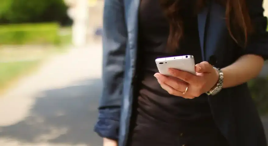 Kobieta z telefonem w dłoni, być może szuka przykładów uporczywego nękania w internecie.
