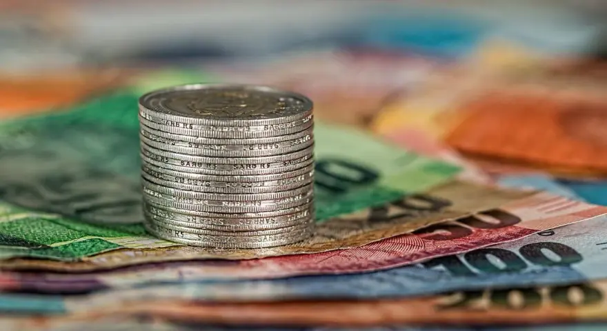 Stos monet na kolorowych banknotach. W tle widoczne fragmenty banknotów o nominałach 100 i 200, co może nawiązywać do artykułu 278 kpk.