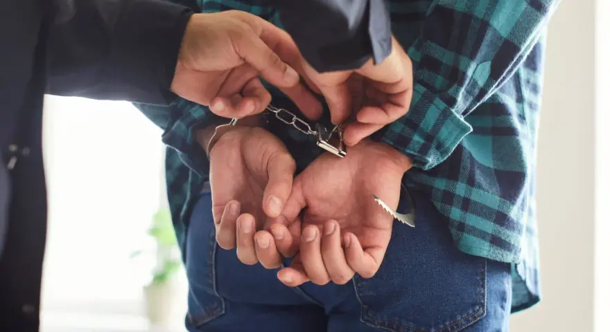 Policjant zakłada kajdanki podejrzanemu o narkotyki. Kaucja za wyjście z aresztu za narkotyki jest zmienna.