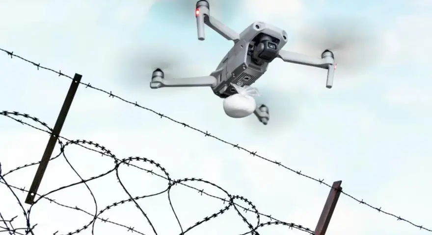 Dron z paczką przelatuje nad drutem kolczastym, niczym rakieta do więzienia dostarczająca przesyłkę.
