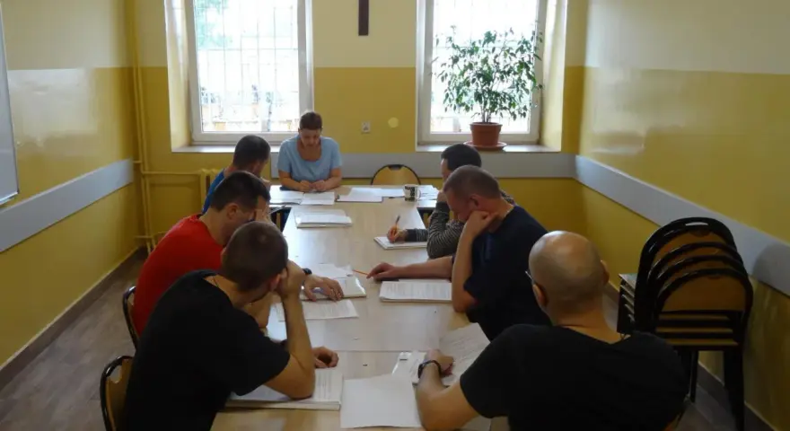 Grupa mężczyzn uczestniczy w zajęciach, które mogą być częścią system programowanego oddziaływania. Siedzą przy stole, studiując dokumenty.