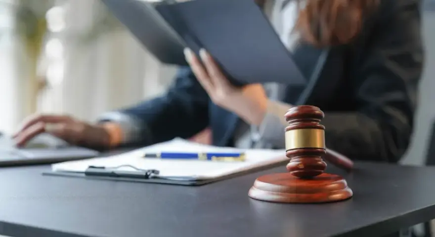 Sądowy młotek i dokumenty na biurku. Prawnik w tle studiuje akta, zastanawiając się, czy radca prawny może być obrońcą.