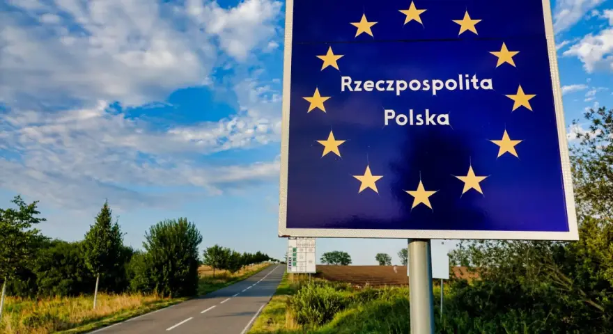 Granica Polski. Znak z gwiazdami Unii Europejskiej i napisem "Rzeczpospolita Polska". Droga prowadzi w głąb kraju, gdzie można złożyć wniosek o uchylenie zakazu opuszczania kraju.