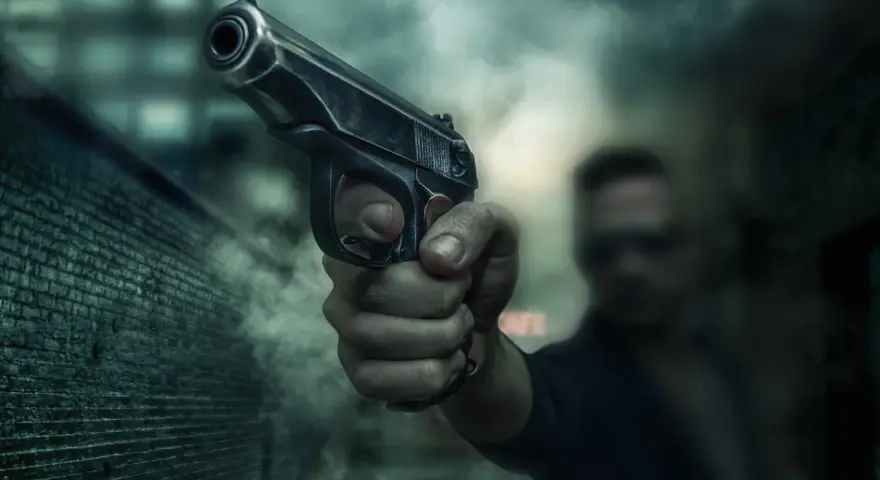 Dłoń trzyma pistolet, gotowa do strzału. Scena sugeruje sytuację z art. 64 par. 2 kk, gdzie groźba użycia broni może być kluczowa.